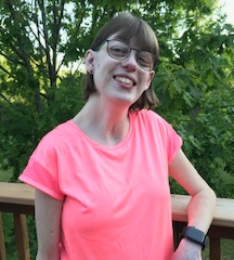 Photo of Stephanie Prysnuk. She has chin-length, light brown hair with bangs. She wears glasses and a bright pink t-shirt.